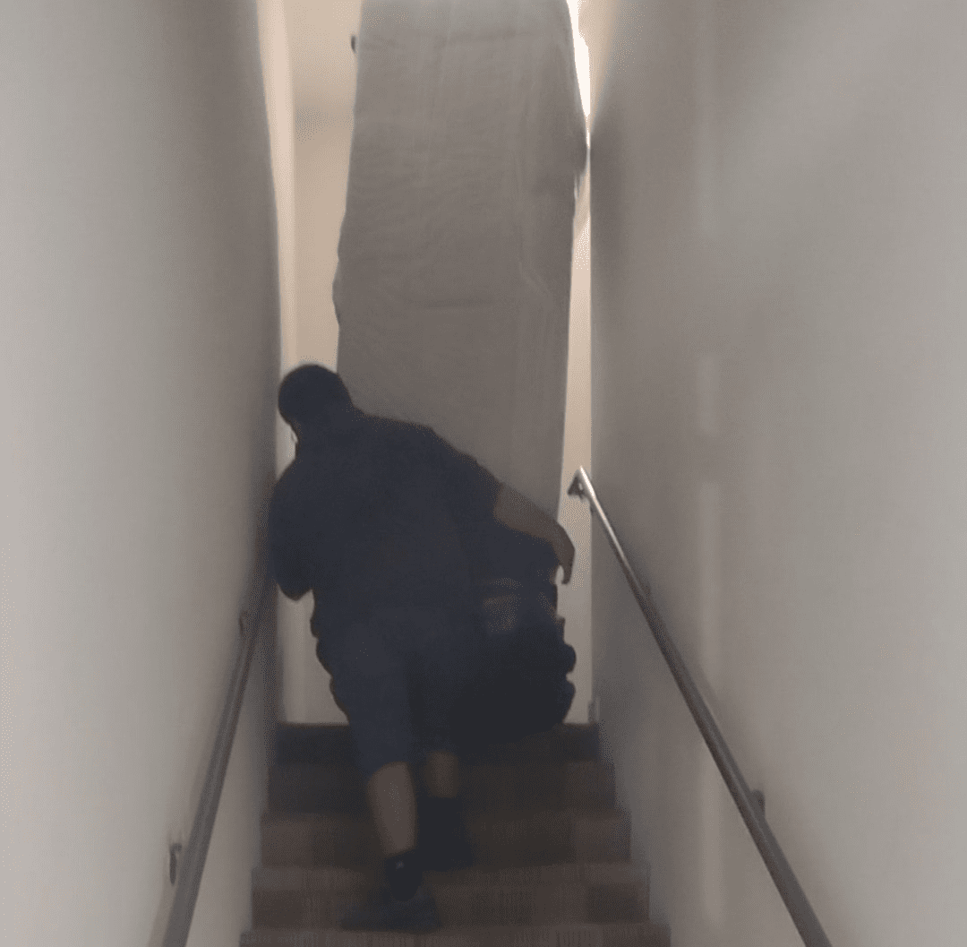 A man carrying a large piece of furniture down the stairs